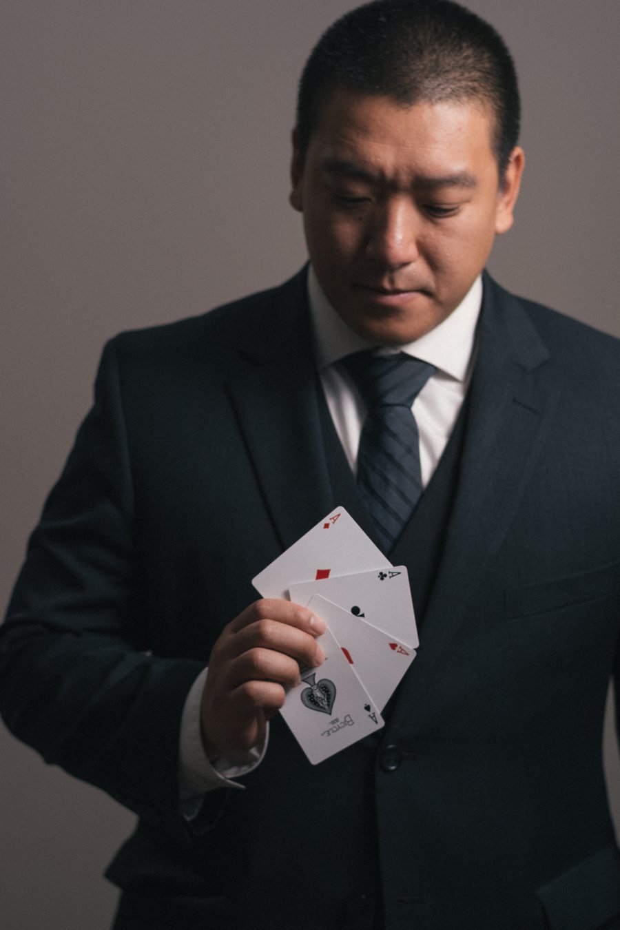 John Ha in a dark suit holding a fan of playing cards
