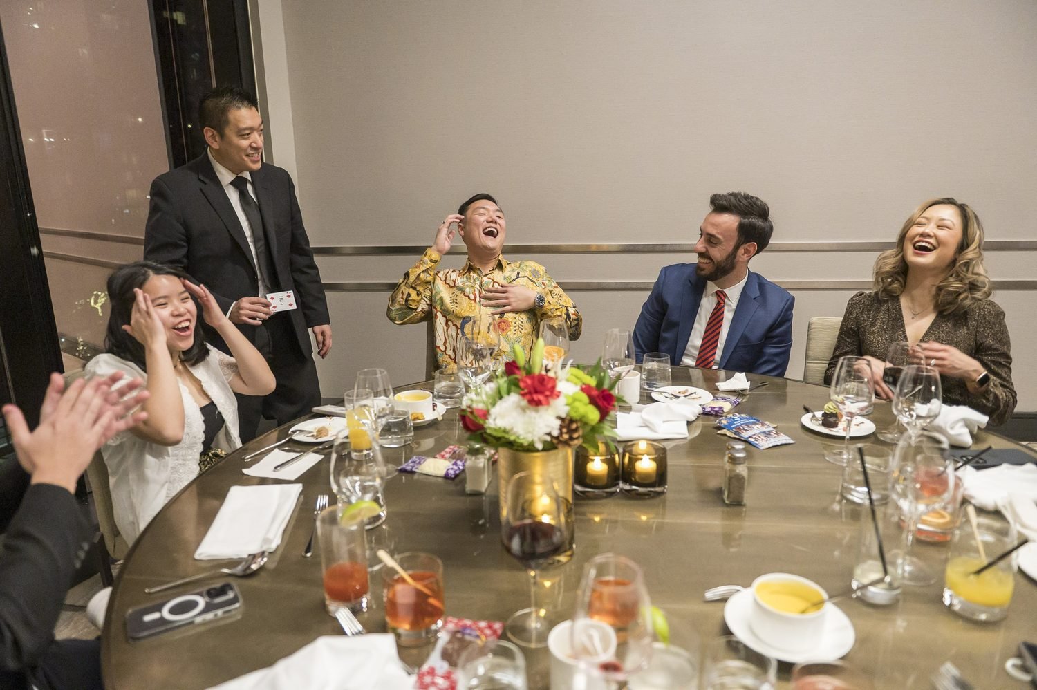 Dinner guests laughing as John performs close-up magic
